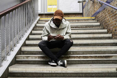 Mann sitzt auf einer Treppe und schaut auf sein Handy - IGGF01371