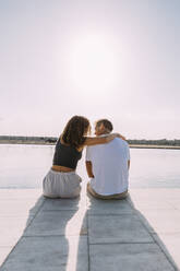 Rückansicht eines jungen Paares, das auf einem Pier am Meer sitzt - MOSF00063