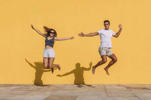 Young couple jumping in front of a yellow wall - MOSF00074