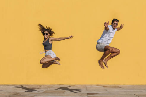 Young couple jumping in front of a yellow wall - MOSF00075
