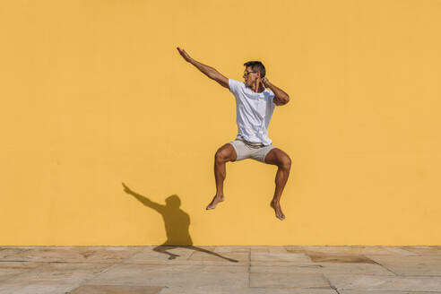 Young man jumping in front of a yellow wall - MOSF00076