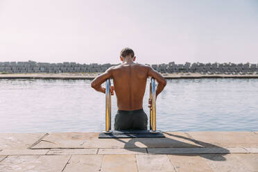 Young man getting into the water from jetty - MOSF00080