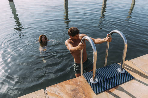 Young man getting out of the water onto a jetty - MOSF00085