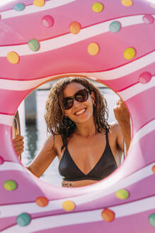 Portrait of happy young woman behind inflatable float in donut shape - MOSF00095