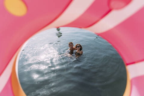 Junges Paar beim Baden im Meer hinter aufblasbarem Schwimmer in Donut-Form, lizenzfreies Stockfoto