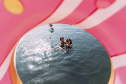 Young couple bathing in the sea behind inflatable float in donut shape - MOSF00096