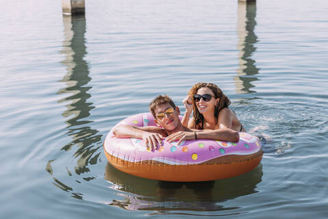 Junges Paar beim Baden im Meer auf einem aufblasbaren Schwimmer in Donut-Form, lizenzfreies Stockfoto