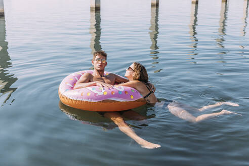 Young couple bathing in the sea on inflatable float in donut shape - MOSF00098