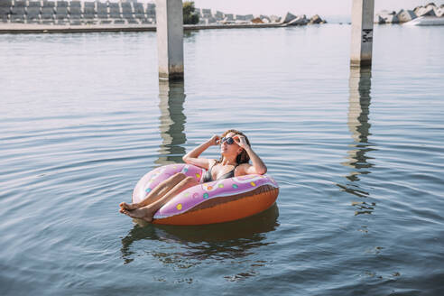 Young woman bathing in the sea on inflatable float in donut shape - MOSF00099