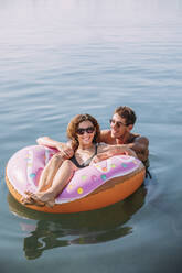 Glückliches junges Paar beim Baden im Meer auf einem aufblasbaren Schwimmer in Donut-Form - MOSF00100