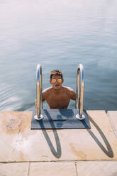 Portrait of young man wearing sunglasses getting out of the water - MOSF00101