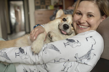 Porträt einer glücklichen Frau, die mit ihrem Hund zu Hause kuschelt - VPIF01601
