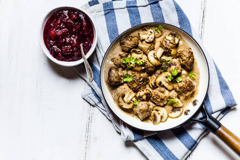 Bratpfanne mit schwedischen Kottbullar-Fleischbällchen in Pilzsoße und Schüssel mit pürierten Preiselbeeren - SBDF04054