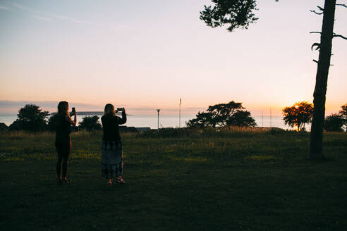 Frauen fotografieren Sonnenuntergang am Meer - JOHF03005