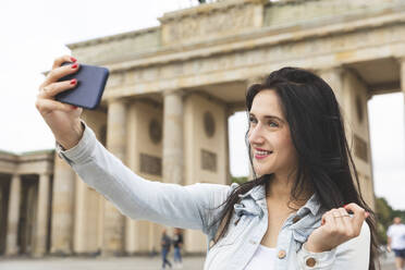 Glückliche junge Frau macht ein Selfie am Brandenburger Tor, Berlin, Deutschland - WPEF02038