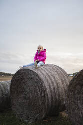 Girl sitting on bale of hay - JOHF03489