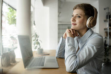 Geschäftsfrau mit Laptop und Kopfhörern in einem Cafe - KNSF06751