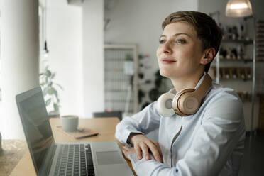 Geschäftsfrau mit Laptop und Kopfhörern in einem Cafe - KNSF06752