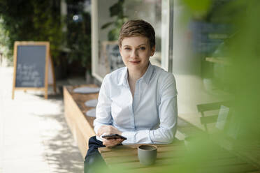 Portrait of smiling businesswoman with cell phone at a cafe - KNSF06762