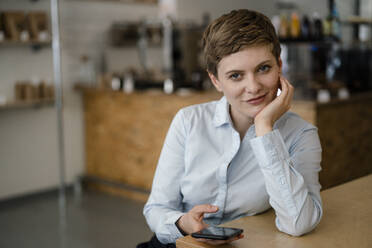 Portrait of a confident woman with cell phone in a cafe - KNSF06776