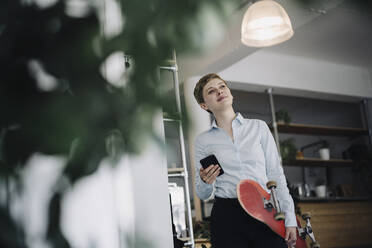 Businesswoman with cell phone and skateboard in a cafe - KNSF06778