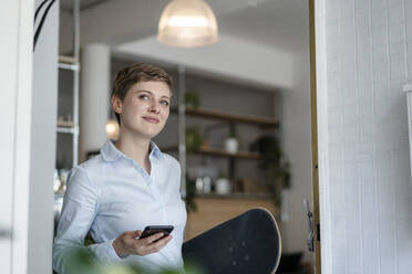 Businesswoman with cell phone and skateboard in a cafe - KNSF06780