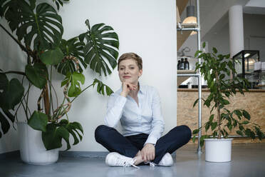 Porträt einer Geschäftsfrau, die auf dem Boden sitzt und von Pflanzen umgeben ist - KNSF06799