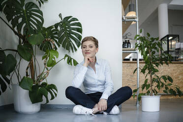 Portrait of a businesswoman sitting on the floor surrounded by plants - KNSF06799