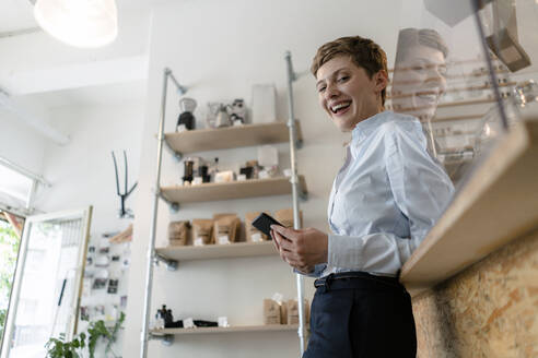 Porträt einer glücklichen Geschäftsfrau mit Mobiltelefon in einem Cafe - KNSF06801