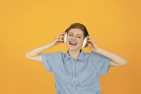 Porträt einer glücklichen Frau, die Musik hört, mit orangefarbenem Hintergrund - KNSF06813