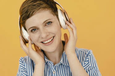 Portrait of happy woman listening to music with orange background - KNSF06815