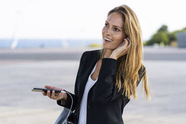 Happy businesswoman with smartphone and earphones outdoors - GIOF07183