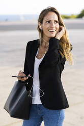 Happy businesswoman with smartphone and earphones outdoors - GIOF07184
