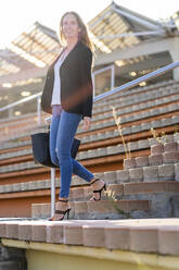Businesswoman with a handbag walking down stairs - GIOF07195