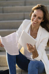 Geschäftsfrau sitzt mit Papier und Tablet auf einer Treppe - GIOF07204