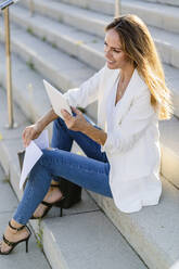 Businesswoman sitting on stairs with paper and tablet - GIOF07205