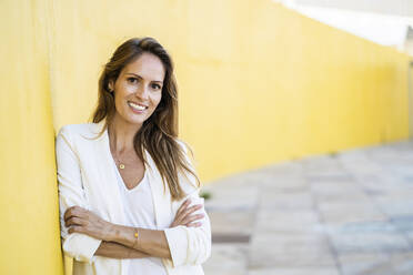 Porträt einer lächelnden Frau, die sich gegen eine gelbe Wand lehnt - GIOF07211