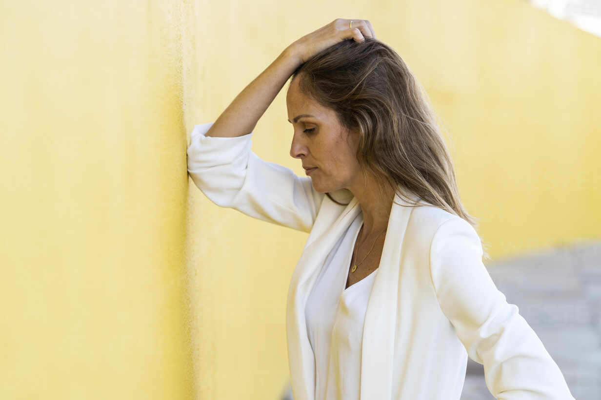 Desperate woman leaning against a yellow wall stock photo