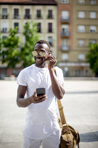 Smiling young man using smartphone and ear phones stock photo