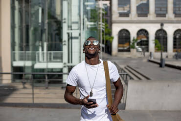 Smiling young man using smartphone and ear phones - CJMF00143