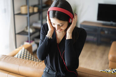 Lächelnde junge Frau, die zu Hause mit Kopfhörern Musik hört - GIOF07219