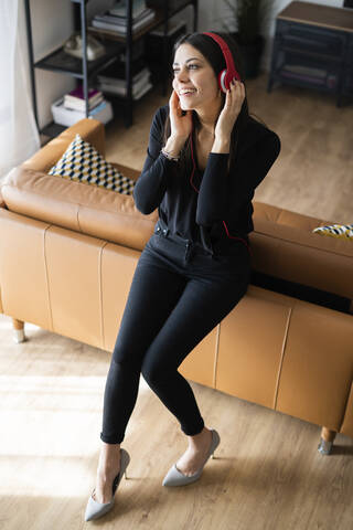 Porträt einer glücklichen jungen Frau, die zu Hause mit Kopfhörern Musik hört, lizenzfreies Stockfoto