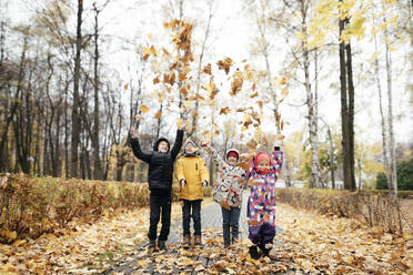 Group of four kids playing with autumn leaves - EYAF00562