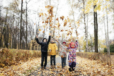 Gruppe von vier Kindern, die mit Herbstblättern spielen - EYAF00562