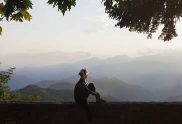 Woman sitting and looking at the mountains - JOHF03657
