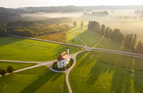 Deutschland, Bayern, Dietramszell, Luftaufnahme von Feldern und der Kirche St. Leonhard bei nebligem Morgengrauen - LHF00724