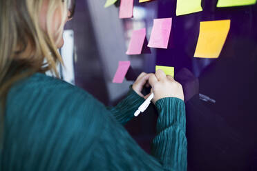 Woman writing on post-it - JOHF03873