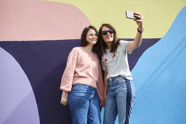 Zwei junge Frauen machen ein Selfie vor einer bemalten Wand - JOHF03950