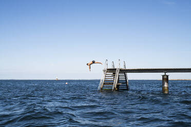 Man jumping into sea from pier - JOHF03957