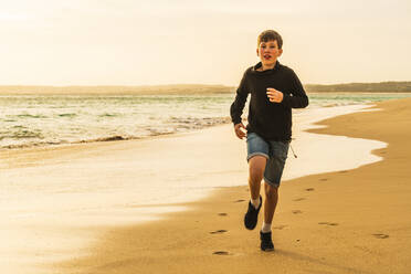 Junge läuft am Strand bei Sonnenuntergang - JOHF03978